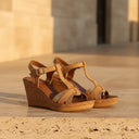 André camel leather wedge sandals with T-strap, buckle closure, and cork wedge heel with glitter details.