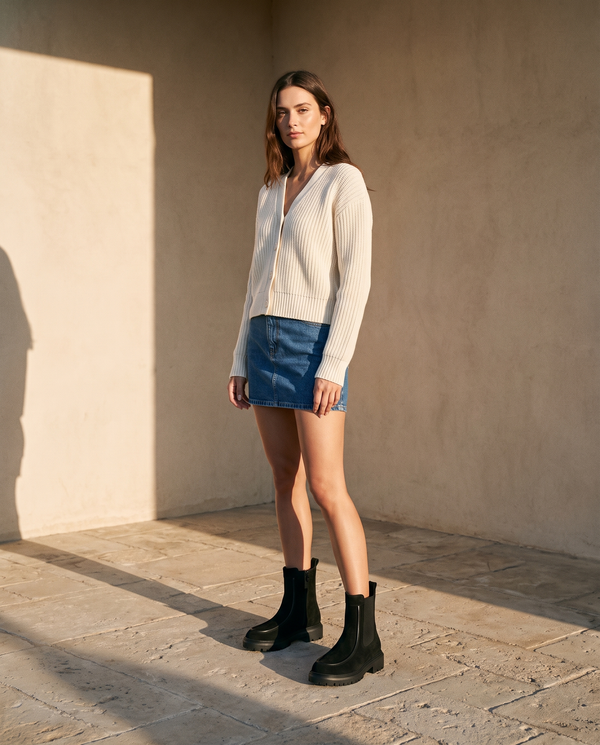 Boots CASSIE noires portées avec une jupe en jean sur une terrasse en pierre — A by André