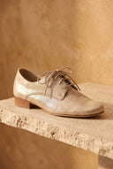André Derby COMPLICE or en cuir véritable, couleur doré, avec lacets et talon plat. Style chic et lumineux.