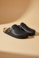 André mules FOLIGNY en cuir noir mat avec boucle métallique et semelle liège anatomique. Chaussures homme confortables et pratiques.