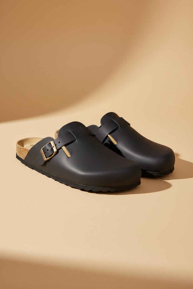 André mules FOLIGNY en cuir noir mat avec boucle métallique et semelle liège anatomique. Chaussures homme confortables et pratiques.
