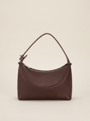 Sac demi-lune Miralie marron posé sur une marche en pierre de travertin, fond ivoire