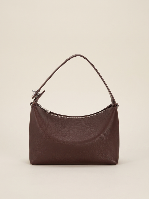 Sac demi-lune Miralie marron posé sur une marche en pierre de travertin, fond ivoire