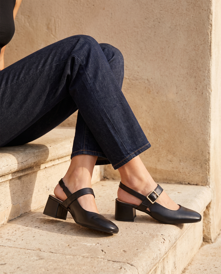 Slingback MONA noire portée, assise sur une marche en pierre