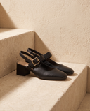 Slingback MONA noire posée sur une marche en pierre, mur enduit beige
