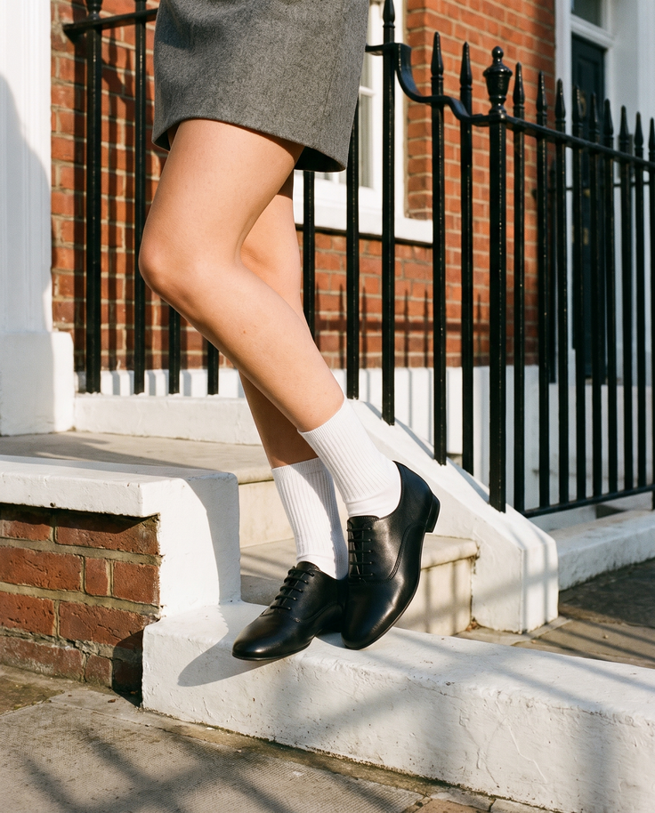 Derby NINI noir porté, gros plan, un pied posé sur la marche d'une maison londonienne