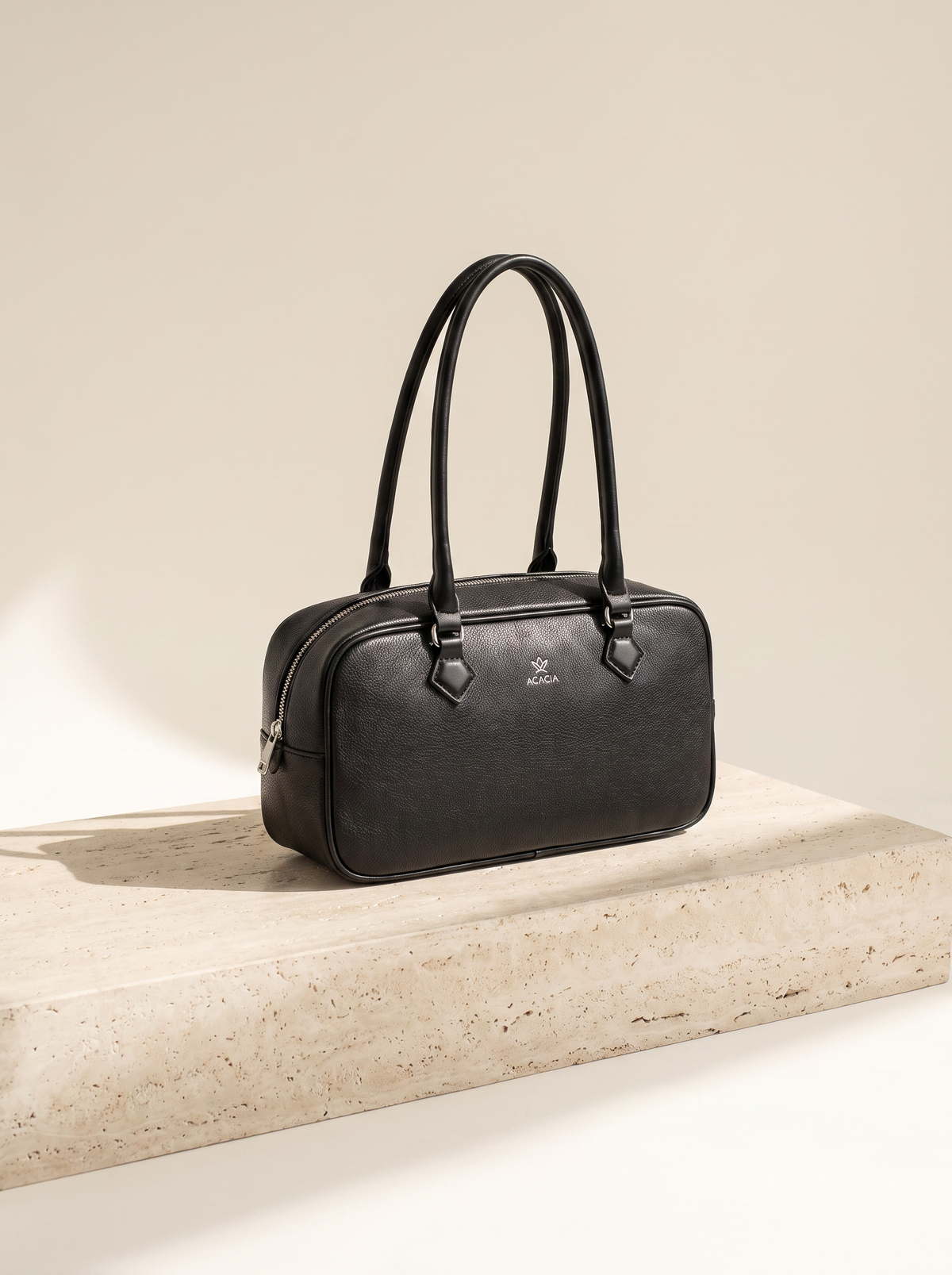 Sac bowling Noélie noir posé sur une marche en pierre de travertin, fond ivoire
