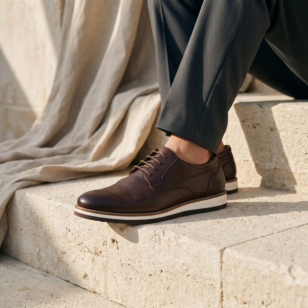 Chaussures de ville André Norwich marron en cuir avec semelle contrastante, portées sur des marches en pierre.