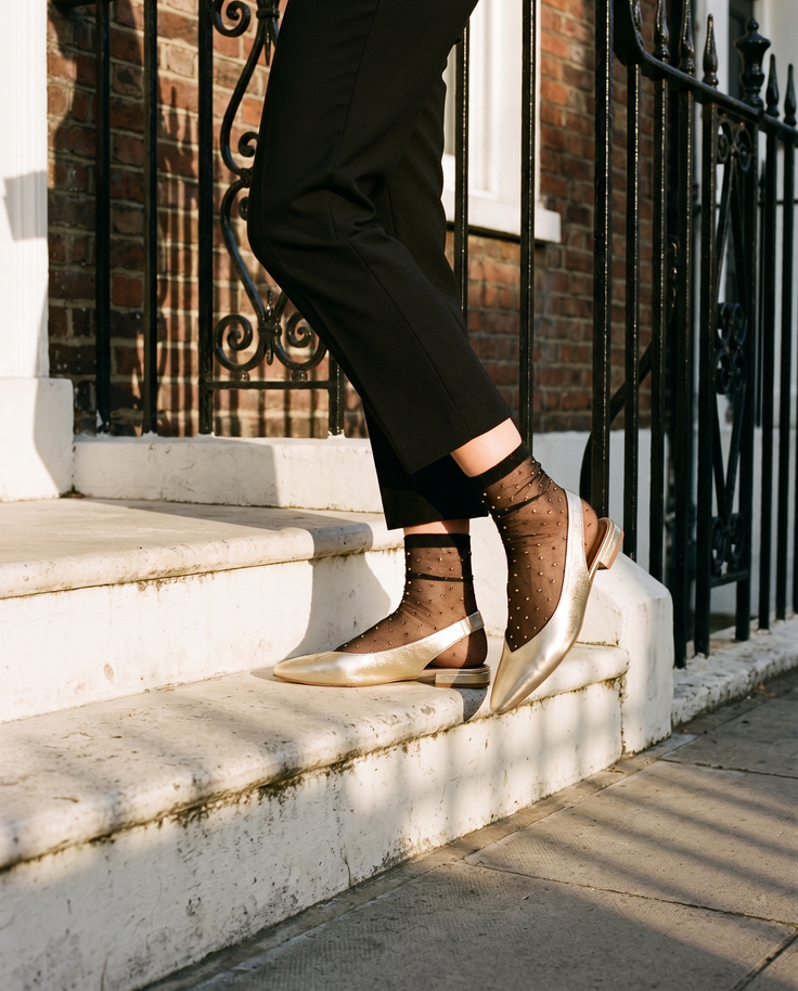 Slingback ROSEE dorée portée, gros plan, un pied posé sur la marche d'une maison londonienne