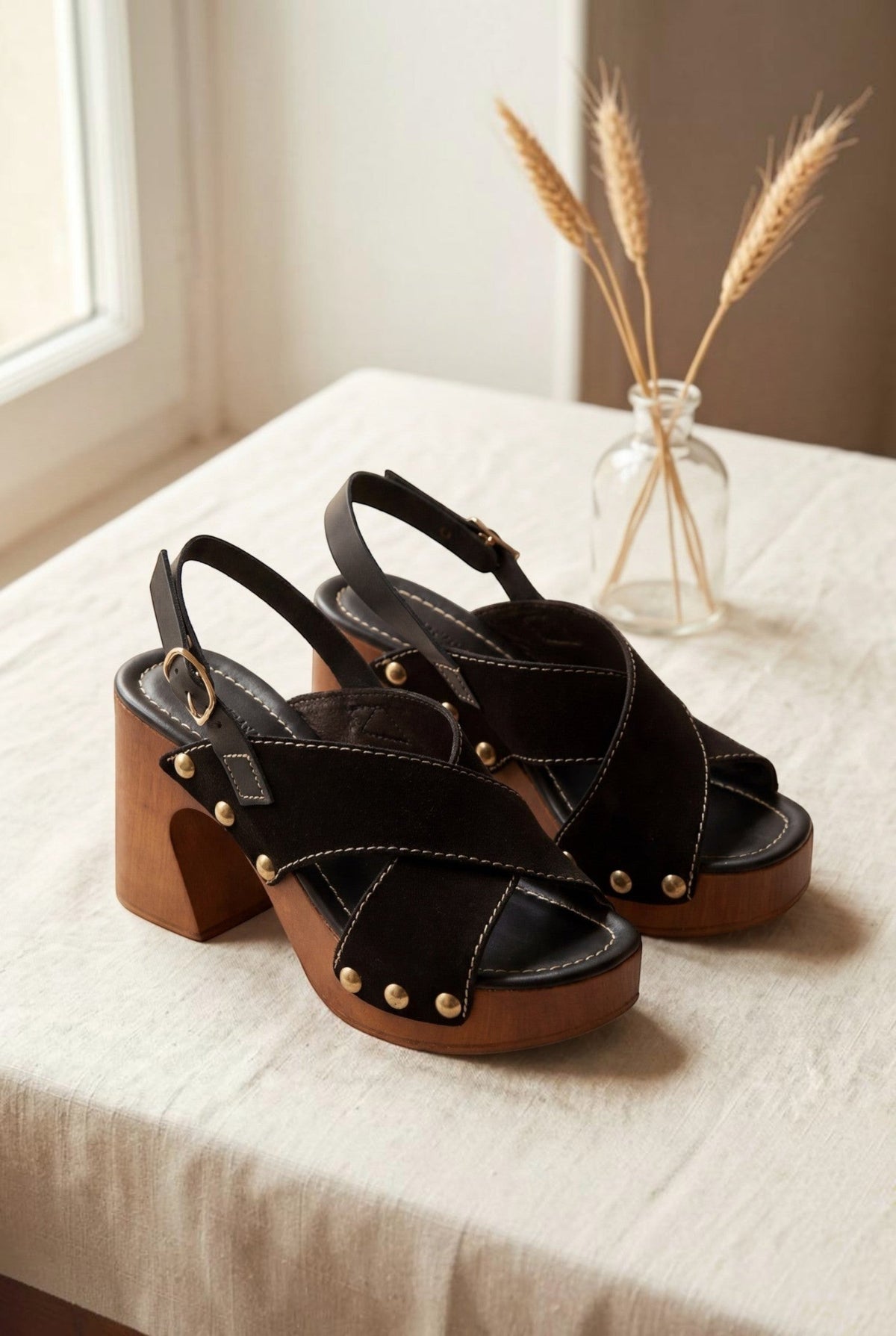 Sabots noirs en suède avec brides croisées, semelle en bois et clous dorés. Talon bloc de 9 cm. Marque André.